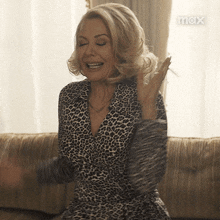 a woman wearing a leopard print dress is sitting on a couch with her arms outstretched