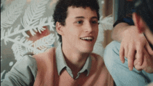 a young man wearing a pink vest is smiling in front of a window with snowflakes on it