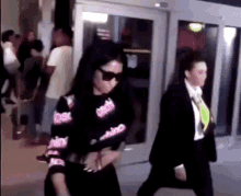 a woman wearing sunglasses and a sweater with the word barbie on it is walking down the street .