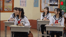 a group of girls are sitting at desks in a classroom with a free fire x poster on the wall behind them