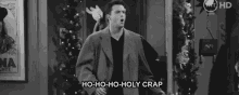 a black and white photo of a man in a suit standing in front of a christmas tree and saying ho ho ho holy crap