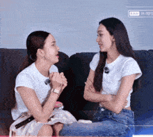 two women are sitting on a couch with their arms crossed and one of them has a watch on her wrist