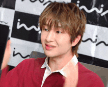 a young man wearing a red shirt and a white shirt stands in front of a black and white checkered backdrop that says in