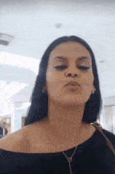 a woman with long black hair is blowing a kiss while wearing a black off the shoulder top .