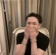 a man is sitting in a chair with his hands on his face and laughing .