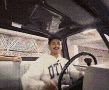 a man in a white sweatshirt with the word dtv on it is driving a car