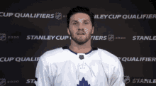 a hockey player stands in front of a wall that says stanley cup qualifiers on it