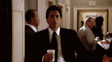 a man in a suit and tie holds a cup in front of a door that says exit