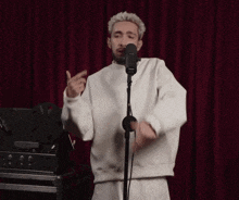 a man singing into a microphone with a red curtain behind him