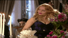 a woman in a purple dress is standing in front of a table with candles and flowers