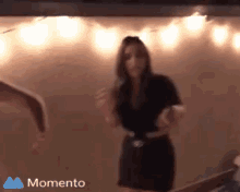 a woman in a black dress is dancing with a momento logo in the background