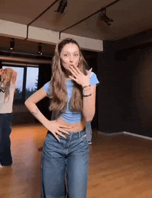 a woman in a blue crop top and blue jeans is dancing in a room .