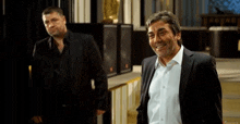 two men in suits and shirts are standing next to each other in a room .