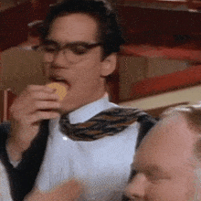 a man wearing glasses and a tie is eating a cookie