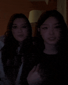 two women are covering their mouths with their hands in a dark room