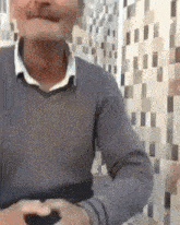 a man in a grey sweater and white shirt is sitting in front of a wall .