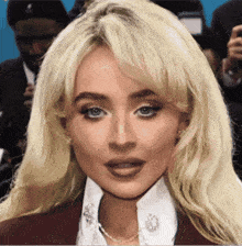 a woman with blonde hair and blue eyes is wearing a white shirt and a red jacket