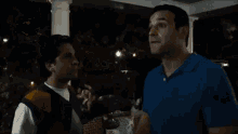 two men are standing on a porch at night talking to each other .