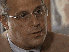 a man wearing glasses and a tan suit looks at the camera
