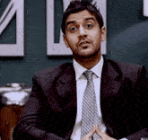 a man in a suit and tie is sitting in front of a sign that says ' a ' on it