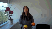a woman holding two fruits in front of a potted plant