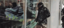 a man in a black jacket and goggles is walking in front of a store window with a picture of a shoe on it .