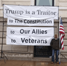 a man is standing in front of a sign that says trump is a traitor to the constitution to our allies to veterans