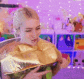 a woman in a gold costume is sitting in front of a purple wall holding a gold bag .