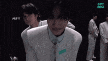 a group of young men are standing in a dark room and one of them is wearing a white suit with a name tag on it