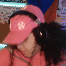 a woman wearing headphones and a pink hat with the letter h on it looks at the camera