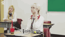 a girl sitting at a desk in a classroom with a twice logo on the wall behind her