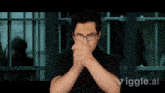 a man with glasses is covering his face with his hands in front of a prison cell with the words vigge.ai visible
