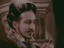 a man with a beard and mustache is wearing a black hat with feathers on it .