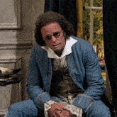 a man wearing sunglasses and a blue jacket sits on a chair