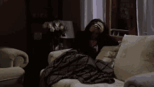 a woman is sitting on a couch with a plaid blanket on her lap