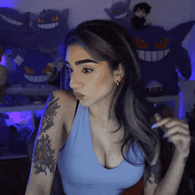a woman in a blue tank top with a tattoo on her arm is standing in front of stuffed animals .