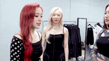 three women are standing next to each other in a room with clothes hanging on a rack .