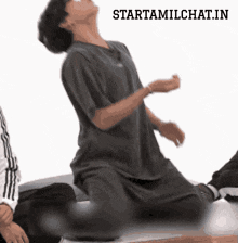 a man in a gray shirt is kneeling down with his arms outstretched in front of a starttamilchat.in sticker