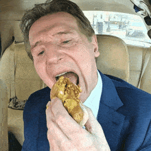 a man in a blue suit and white shirt is eating a hot dog