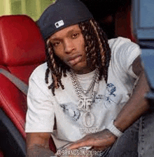 a young man with dreadlocks is sitting in a car wearing a hat and a t-shirt .