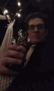 a man with glasses is drinking from a bottle in a dark room