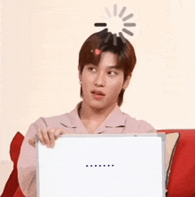 a man is sitting on a couch holding a white board with a loading screen on his head .