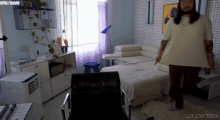 a man in a white shirt is standing in a living room with a purple curtain and a sign that says loucodeck