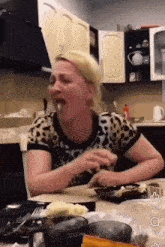 a woman in a leopard print shirt is sitting at a kitchen table eating food