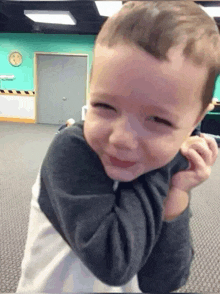 a little boy is smiling in a room with a clock on the wall behind him