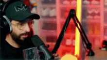 a man with a beard is wearing headphones and a hat while sitting in front of a microphone .