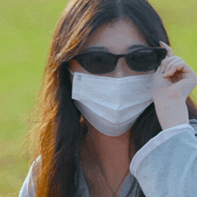 a woman wearing a mask and sunglasses looks at the camera