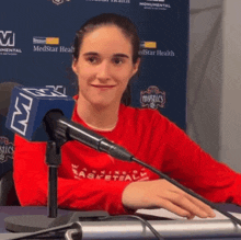 a woman sitting in front of a microphone wearing a red basketball shirt