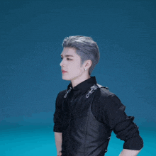 a man in a black jacket stands with his hands on his hips and says " what ? "