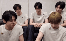 a group of young men wearing white t-shirts are sitting on a couch and smiling